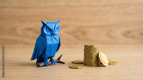 Blue paper owl ai agent for business near coin stack, finance concept, on wooden surface