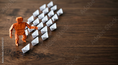 Ai agent for business guiding paper team on wooden desk with orange paper figure and white paper boats