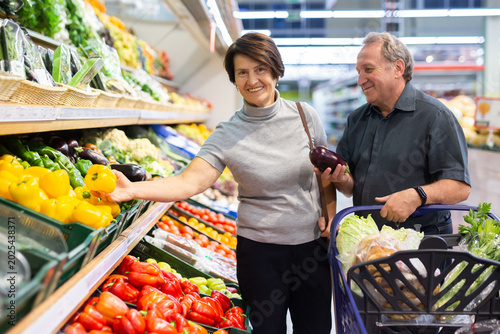 Quadro su tela Mature woman and man selecting vegetables in greengrocer