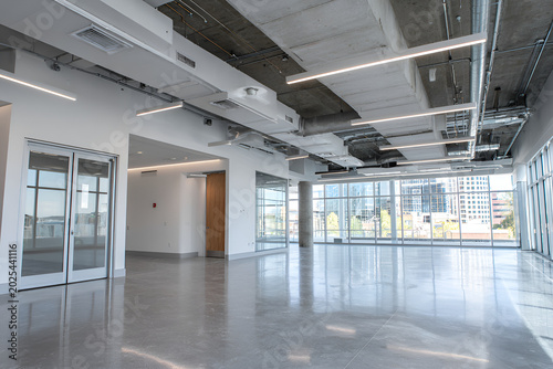 Expansive interior shot showcasing a modern, empty commercial space with polished concrete floors and large windows. The ceiling reveals exposed ductwork