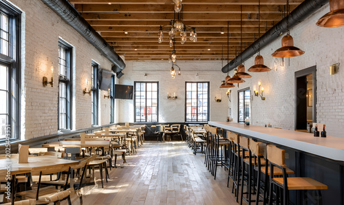 An interior shot, featuring a long bar and multiple dining tables, illuminated by overhead and wall lighting