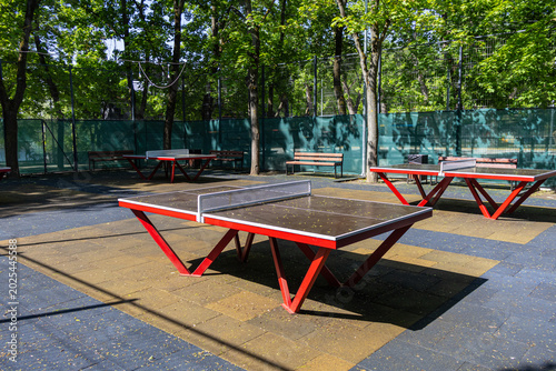 Outdoor table tennis area in public park with red professional ping pong tables.
