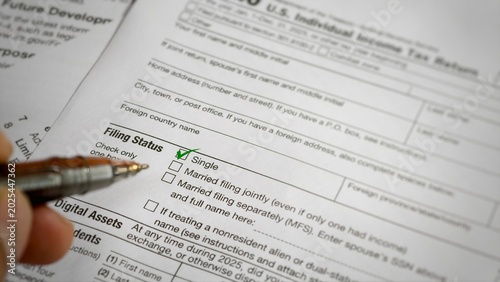 A close-up informational view of an IRS Form 1040 U.S. Individual Income Tax Return, showing a hand with a pen pointing to a green checkmark next to the 