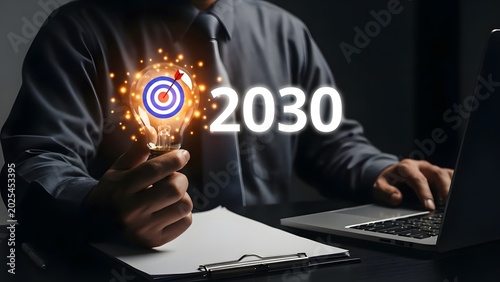 Hand firmly grasps a glowing light bulb, containing a target icon, beside the year 