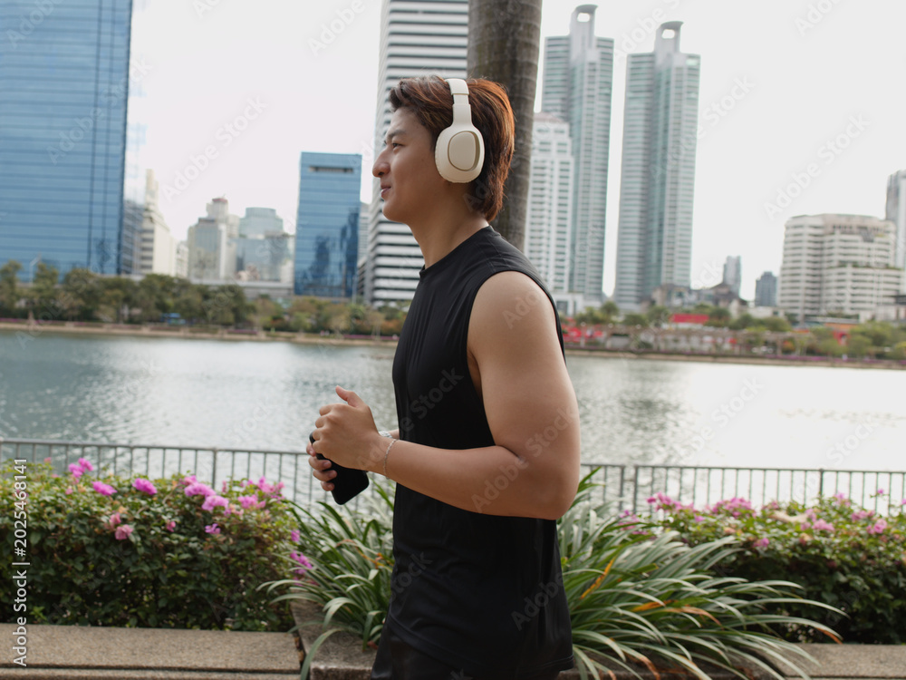 Obraz premium Asian Man Jogging in Benjakitti Park with Bangkok Skyline Background