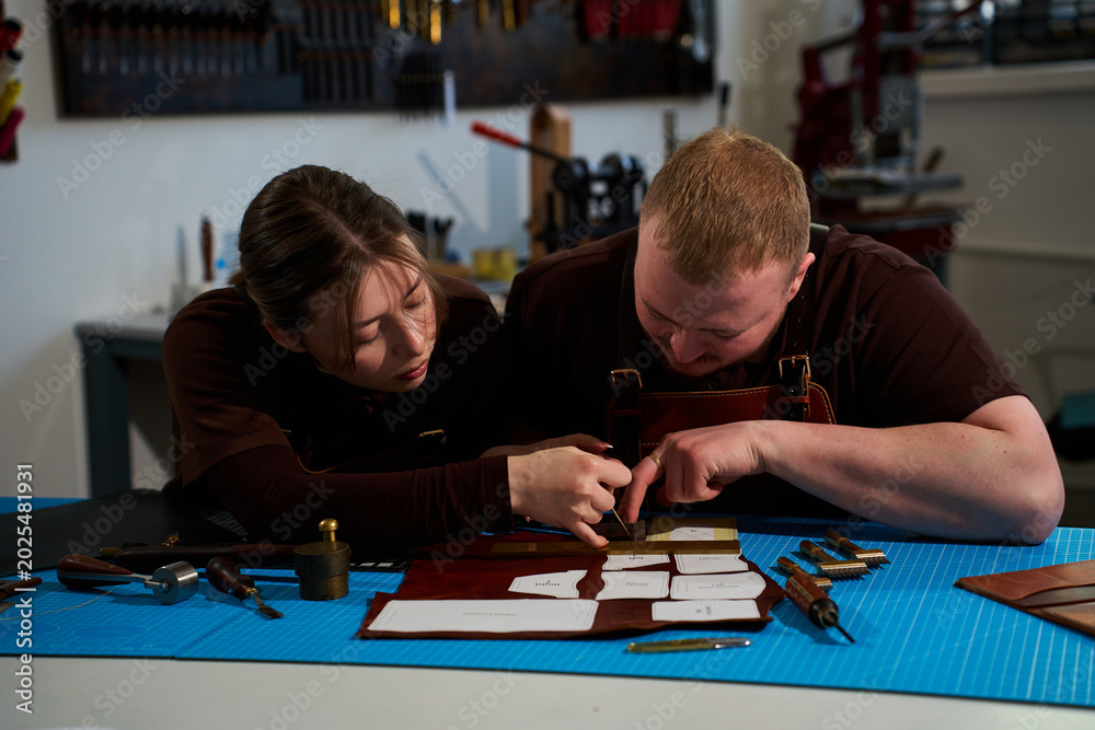 Fototapeta premium Leatherworkers in aprons working with cowhide and paper patterns.