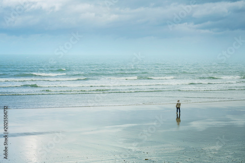 Bilde på lerret Minimalist coastal landscape of a figure reflecting on a vast sandy beach at low tide in Ballyheigue Ireland