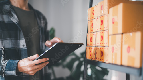 Inventory manager checking ecommerce stock and package organization using tablet in warehouse workspace, supporting logistics management, order tracking, and retail inventory operations.