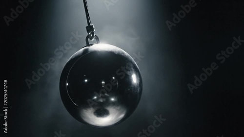 Metallic wrecking ball hanging in dark, smoky spotlight