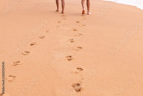 Foto Two pairs of bare feet walk away on a sandy beach, leaving clear footprints in the warm, golden sand