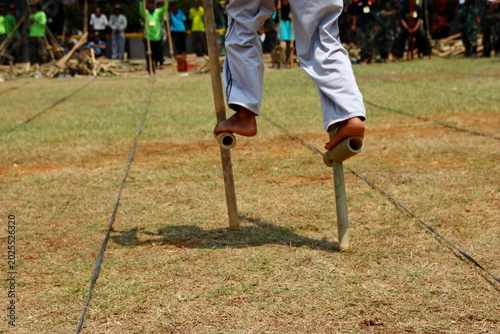 Foto A participant plays traditional bamboo stilts outdoors, highlighting balance, agility, and Indonesian cultural games