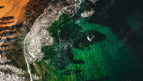 Drone shot aerial view of a beach with waves crashing onto the sand 