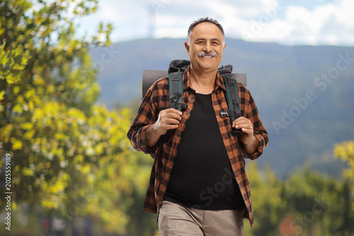 Photos Mature hiker carrying a backpack and walking in a park