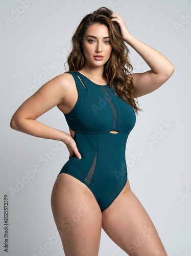 Confident curvy woman elegantly posing in a stylish dark teal one-piece swimsuit, showcasing her natural beauty and empowerment with grace and allure