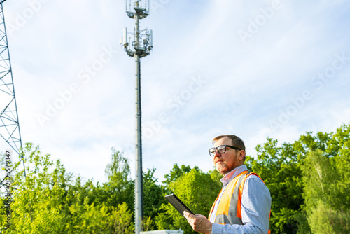Engineer checking technical data on the tablet during maintenance 5G cell tower. Utility technician or environmental inspector conducts an infrastructure audit. 