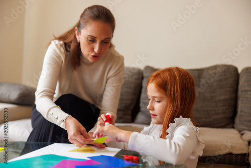 Mother and daughter cutting and gluing collage paper while doing an art project at home for school