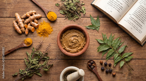 Ayurvedic Ingredients and Ancient Book on Wooden Background