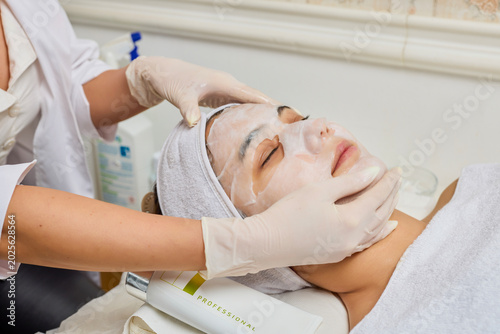 Billede på lærred picture of a young woman at a beauty salon where she is being given a paper mask