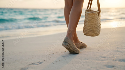 Low Angle View of Woman in Espadrilles Walking on Sandy Beach Carrying Woven Straw Bag at Golden Hour Sunset