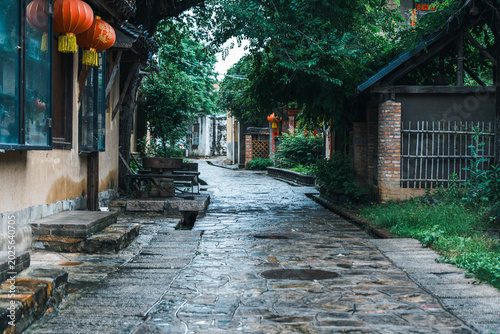 Foto A quiet wet stone paved alley in a traditional Chinese ancient town, lined with rustic wooden buildings, green trees and red lanterns after rain