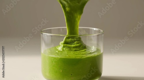 Close-up of vibrant green smoothie (spinach, banana, avocado) being poured into a clear glass