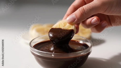 Close-up slow motion of frozen banana slices dipped into melted dark chocolate