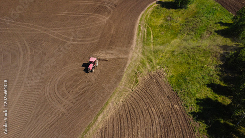 Fotografie Aerial View of a Red Tractor Harrowing a Large Agricultural Field
