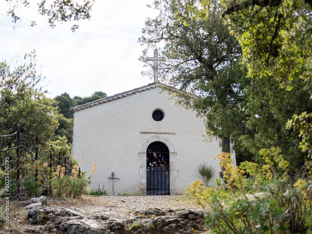 Fototapeta premium pignon de chapelle médiévale en provence, sur une colline, au milieu de la végétation, avec croix forgée sur le toit