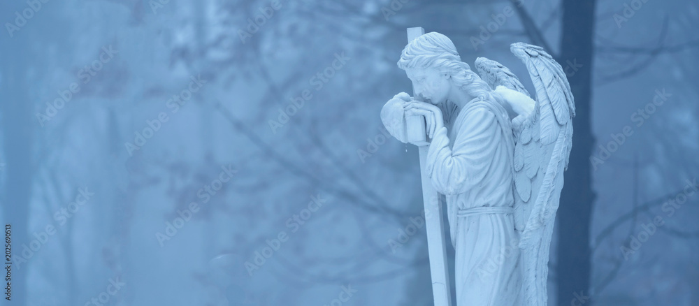 Fototapeta premium White angel statue standing alone in a mysterious foggy forest atmosphere