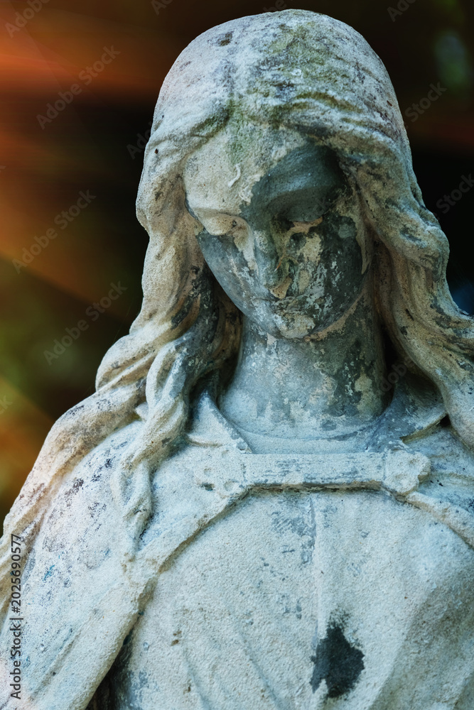 Fototapeta premium Ancient angel statue with weathered face in warm dramatic light, symbolic image of silence, sorrow and eternity