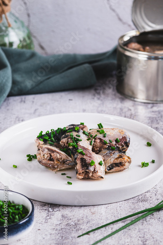 Tableau sur toile Canned sardines with green onions on a plate on the table vertical view