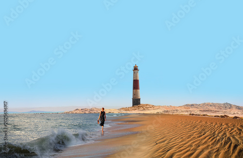 A blonde woman in a black dress walking towards a lighthouse painted red and white on a wavy beach - Amazing red and white lighthouse near Diaz Point  -  Lüderitz, Namibia