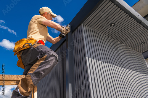 Worker on ladder installing panels on a building under clear blue sky