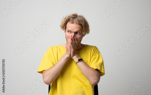 Fotografía Young blond man in a yellow t-shirt covering his nose and mouth with hands, feel