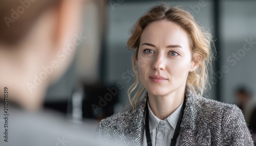 Professional Woman In Gray Jacket And Id Badge Engages In Active Listening And Effective Communication With Colleague In Modern Office Meeting.