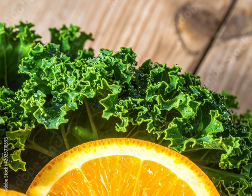 Kale foliage and orange slice placed on wooden table surface