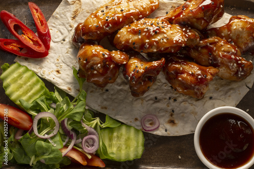 Foto Glazed chicken wings on tortilla wrap, avocado salad, chili slices, sesame seeds