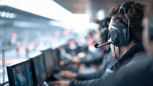 Formula racing engineer using communication headset at pit wall station.