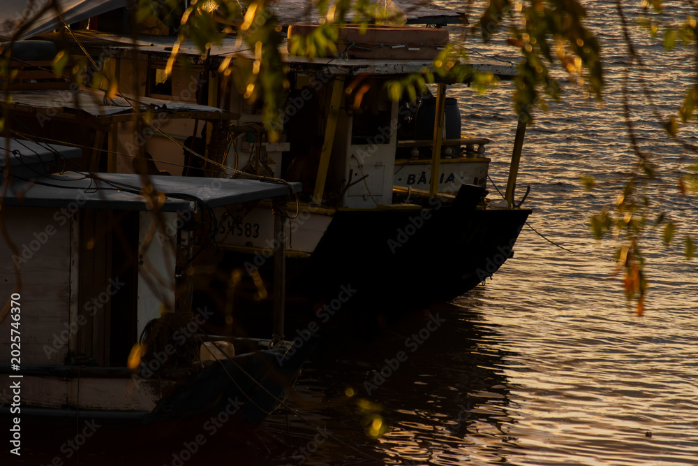Obraz premium High quality tropical sunset landscape at Rio de Contas in Itacare Bahia Brazil featuring a boat crossing calm reflective waters with intense golden sunlight dramatic sky and realistic ocean reflectio