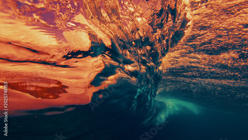 Underwater view of a breaking ocean wave with golden sunset light reflecting through the water surface and dynamic textures.