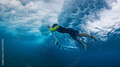 Male surfer performing duck dive underwater on surfboard in clear tropical ocean