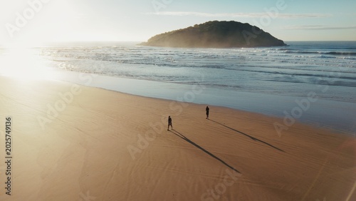 Two persons walk on the wide sandy beach with island on the horizon