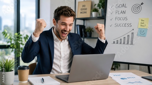 Excited businessman celebrating success in front of laptop at modern office