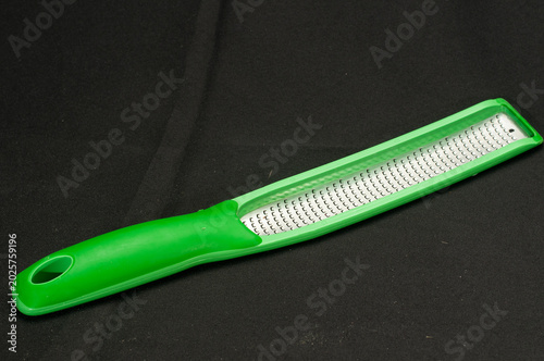 Top view, close distance of, a green handle cheese shredder, on black background, under studio strobe lighting