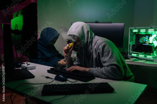 Tableau sur toile Two anonymous hackers in hoodies work on computers in dark room