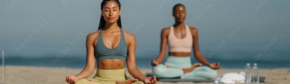 Obraz premium Woman practicing seated yoga meditation on oceanfront sand