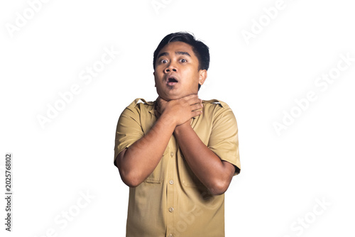 Cuadro en lienzo Panicked young man in a khaki uniform shirt looking at the camera with wide eyes and open mouth while clutching his own neck with both hands in a choking gesture against a white background