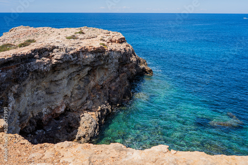 Fotografi Rugged limestone cliff plunging into a vibrant turquoise Mediterranean sea on a