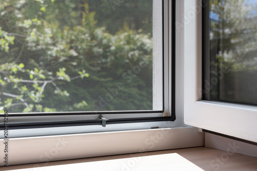 Open window with mosquito net screen, sunlight through mesh, clean home interior, fresh air ventilation concept, window frame detail, natural light indoor background