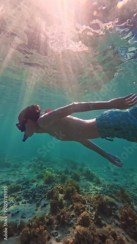  A teenage boy wearing a mask, snorkel, and fins swims underwater in the ocean exploring the underwater world